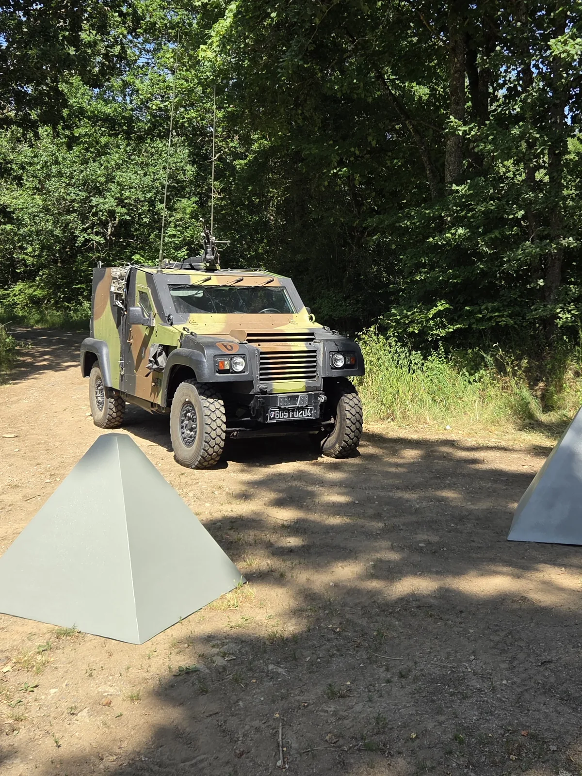 Véhicule blindé arrêté devant des leurres de dents de dragon anti-char sur une piste forestière